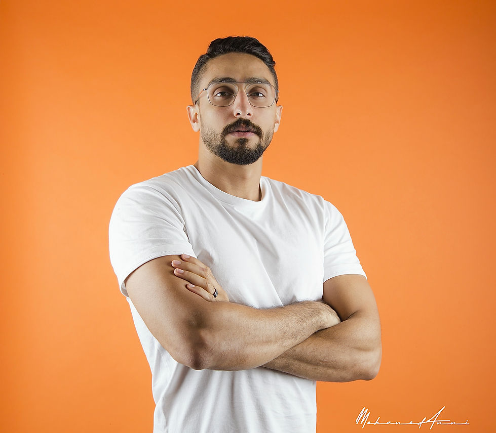 Confident man with glasses crossing his arms against an orange background.